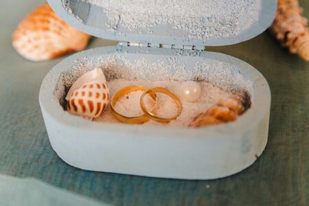 wedding rings in a rustic box with white sand and seashells, for the wedding ceremony or vow renewalの写真素材
