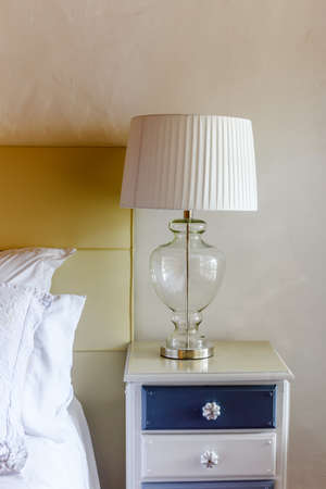 Side table with white lamp in the bedroom with white pillows