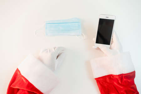 Santa Claus in a medical mask with a smartphone. Online greetings, ordering services for Christmas...