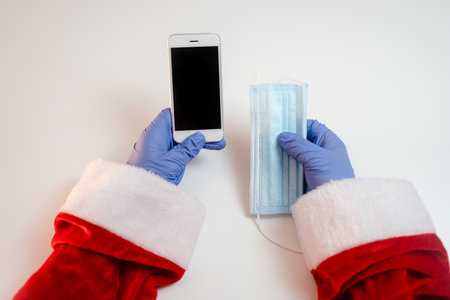 Santa Claus in a medical mask with a smartphone. Online greetings, ordering services for Christmas and new year. Social distance in the coronavirus epidemic, a new reality.の写真素材