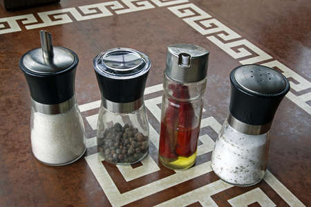 Four transparent cans with sugar, pepper, red hot pepper in oil and salt are on the plastic tableの写真素材