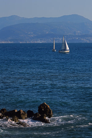 Two of sailing boats floating on the sea against the background of the coast with the mountains near Antibes in France. Great space for writing. With unidentified peopleのeditorial素材