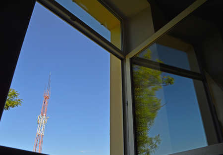 Open window overlooking the sky, tree and mobile phone antenna. Selective focus