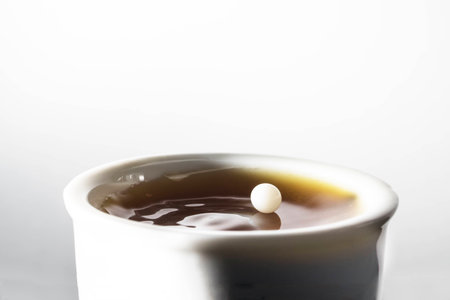 Drop of milk balancing and reflected on top just as it hits a cup of black coffeeの写真素材