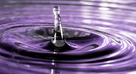 Water drop in the shape of a helter skelter on a rippled purple backgroundの写真素材