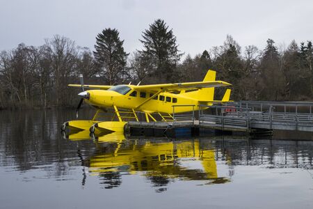 Loch Lomond, Scotland - 2 April 2015 - Yellow Loch Lomond Seaplane reflected in the loch at its mooring on Loch Lomond beside Cameron House Hotelのeditorial素材