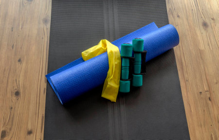 Hand weights, resistance band, and yoga mat on black foam mat on wooden floor backgroundの写真素材