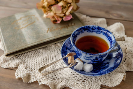 Antique blue and white china cup and saucer with tea and sugar cubes on lace cloth on wooden table...