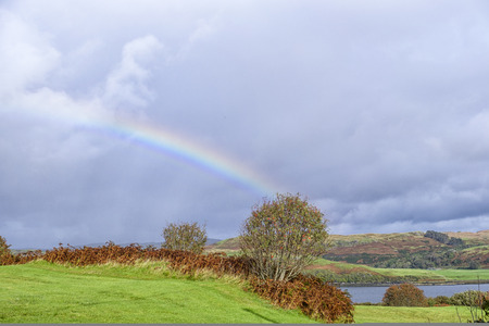 Beautiful colorful rainbow after the rain on stunning remote rural landscape on Isle of Skye Scotland. Loch and heather covered hills in the background.の写真素材