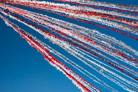 Streaks of colorful red and white garland bunting fluttering in the breeze against clear blue skyの写真素材