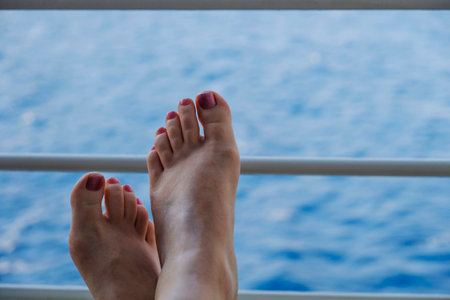 Woman's feet, toes painted with pink nail varnish resting on the railings of a cruise ship with sea backgroundの写真素材