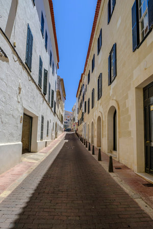 Looking up one of the narrow old streets in Porto Mahon in Minorca with beautiful whitewashed residential  buildings with traditional wooden window shuttersの写真素材