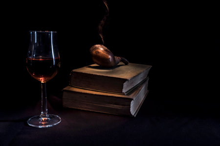 Evening still life scene of smoking pipe, glass of Scotch whisky and old books against black background with copy spaceの写真素材
