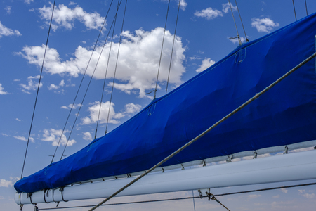 Beautiful bright blue canvas of furles sail against blue sky with white cloudsの写真素材
