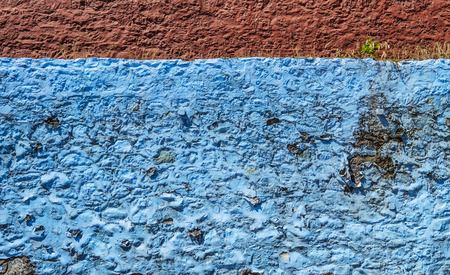 Peeling blue and red paint on roughly textured wall with weeds growingの写真素材
