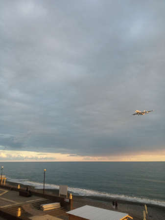 a plane coming in to land over the sea and the beach at sunset