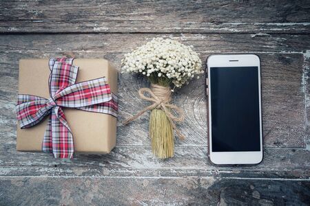 Bouquet flowers, gift box and phone on vintage and old wooden table.の写真素材