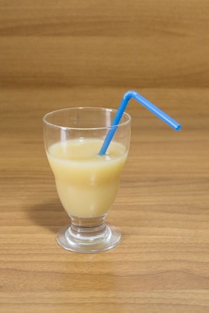 Fruit juice in a glass with a blue straw on a wood table compositionの写真素材