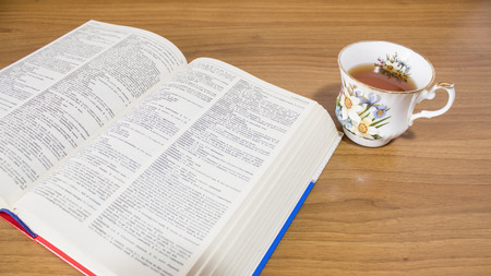 School, an open book and a hot cup of tea on a wood table composition