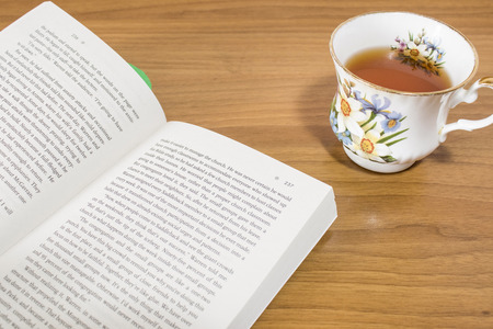 An open book and an hot cup of tea on a wood table compositionの写真素材