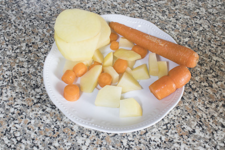 Cut carrots and potatoes on a white plate ready for meal compositionの写真素材