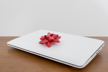 White laptop gift with a red ribbon on a wood table compositionの写真素材