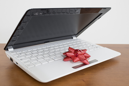 White laptop gift with a red ribbon on a wood table compositionの写真素材