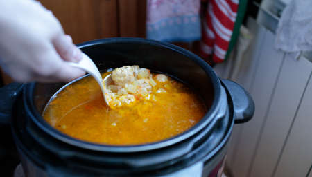 woman stirring with a plastic scoop the soup with meatballs cooked in a slow cookerの写真素材