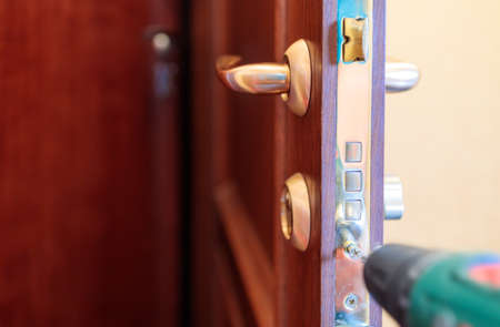 screwing a screw into the lock on the front door using a screw gunの写真素材