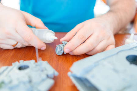 a man assembles a model of a toy tank from plastic, glues a hatch from a tank with an installed...