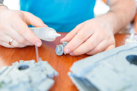 a man assembles a model of a toy tank from plastic, glues a hatch from a tank with an installed machine gunの写真素材