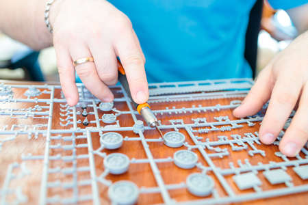 a man collects a model of a toy tank from plastic, cuts off a tank wheel from a setの写真素材