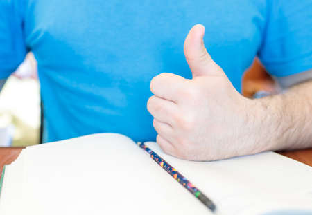 man shows thumbs up near the background of diary and pencilの写真素材
