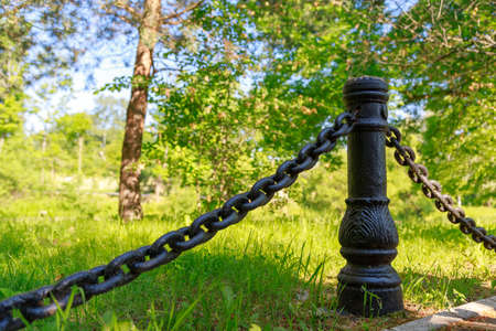 black old post with chains on a background of green grass and woodの写真素材