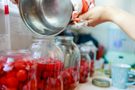 a woman pours hot water into a glass jar where strawberries lie, she makes compoteの写真素材
