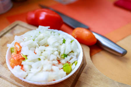 bowl with chopped vegetables and onions stands on a cutting boardの写真素材