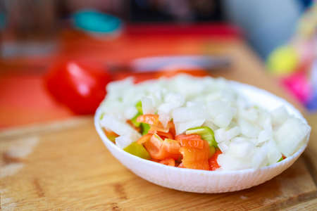 bowl with chopped vegetables and onions stands on a cutting boardの写真素材