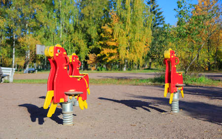 swings in the form of horses in red on the background of benchesの写真素材