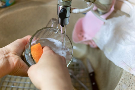 woman washes her glass under running water in the sinkの写真素材