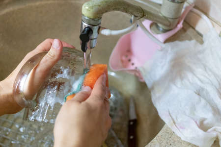 woman washes her glass under running water in the sinkの写真素材