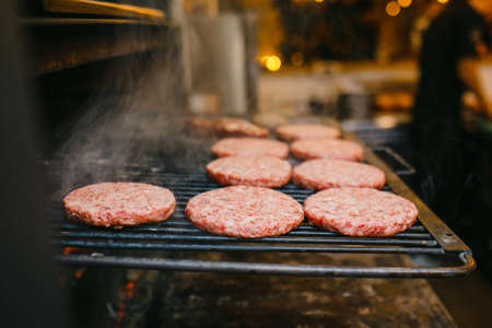 Raw hamburger patties being cooked on a barbecue grill.の写真素材