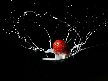 Strawberry creating a splash as it is dropped onto a spoon filled with creamの写真素材
