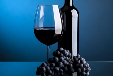 A glass of red wine with bottles on a blue background の写真素材