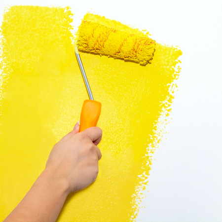 Painting roller on white wall with yellow paint