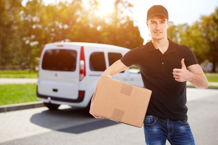 Smiling delivery man holding a cardboard box in sunlight