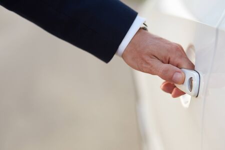 Hand of businessman in formal wear opening a car door