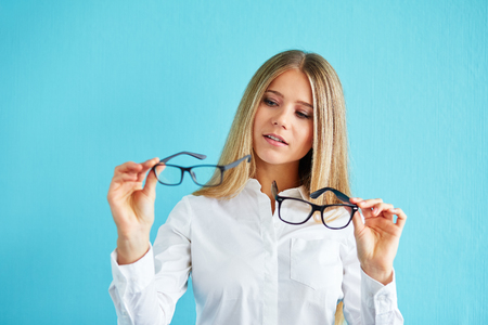 Pensive businesswoman with glasses standing before blue background