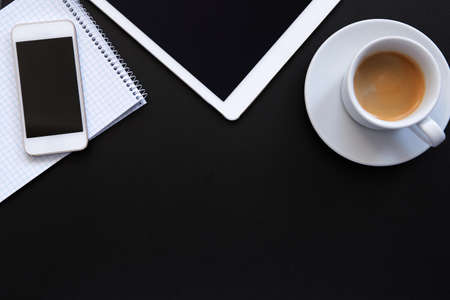 Top view of workplace, tablet with phone, coffee cup and diary on black tableの写真素材