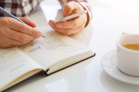 Man sketching web design and holding mobile phone. Toned image with sunlight