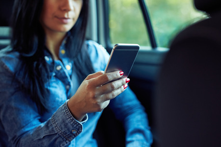 Woman with mobile phone in hand sitting in the car and typing text messageの写真素材